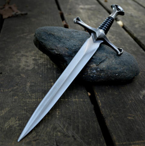 A dagger poised on a rock over a wooden surface.